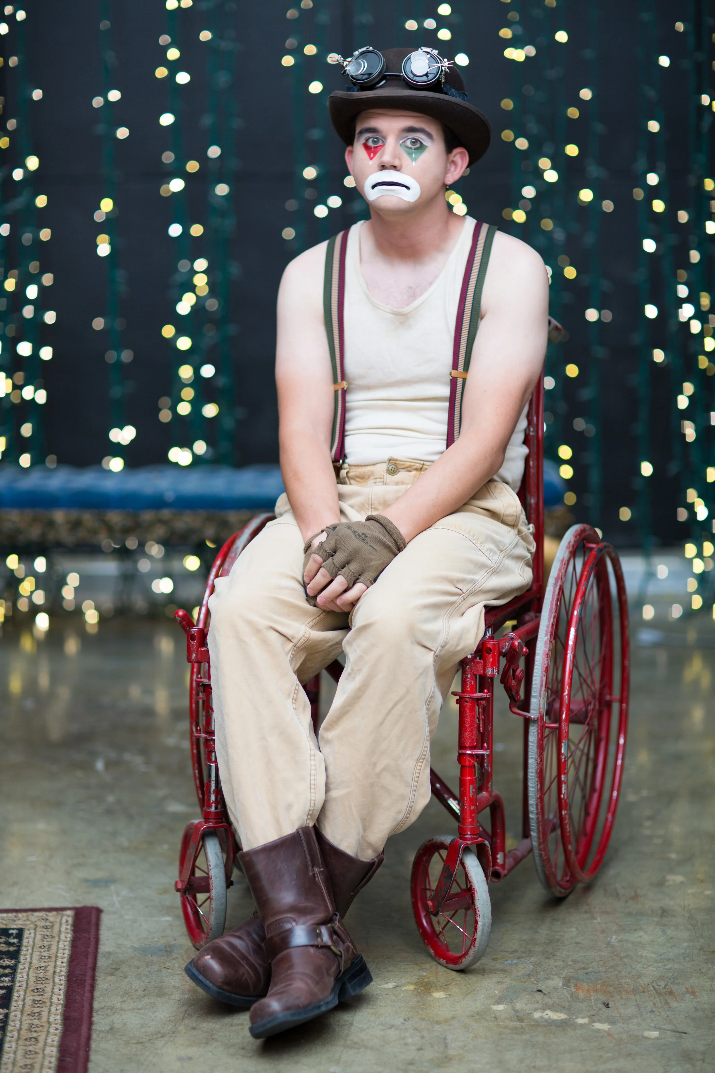 Sad Clown Lee seated in a red wheelchair beneath stage lights