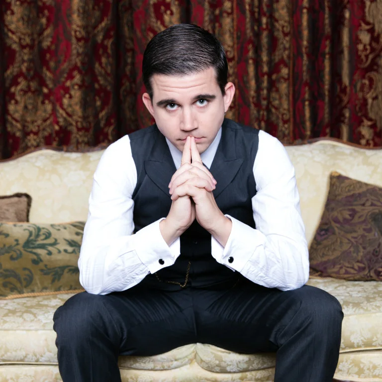 Lee Huff in character seated forward on a vintage couch